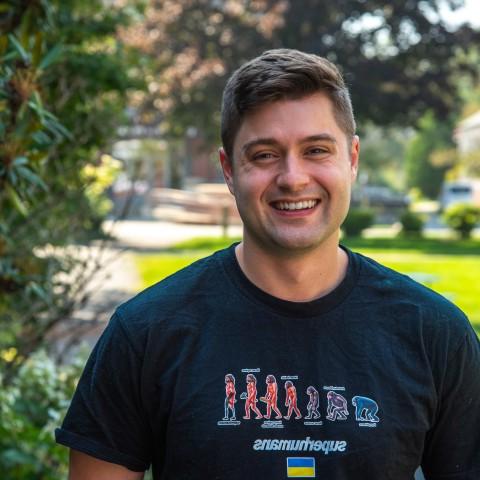 罗伯特·莫特利在正规澳门赌场网络帕克馆外的院子里摆姿势拍照. He wears a shirt that reads "Superhumans," which is the name of the clinic he volunteered at in Ukraine.
